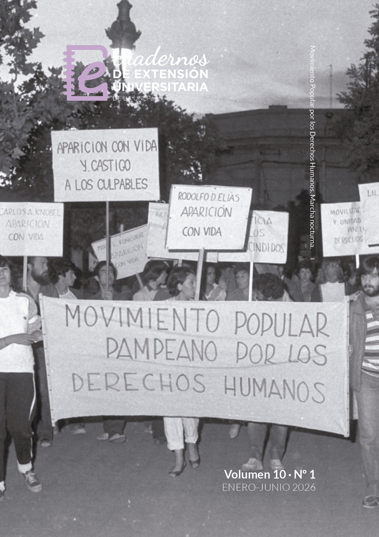 La imagen es una fotografía en blanco y negro de una marcha por los derechos humanos, tomada al aire libre en un paseo arbolado, probablemente al atardecer. En el centro avanza un grupo numeroso de personas que sostiene carteles con reclamos escritos a mano y una gran bandera horizontal con la leyenda “Movimiento Popular Pampeano por los Derechos Humanos”. También se observan pedidos de “Aparición con vida” junto a nombres de personas desaparecidas. La escena transmite un clima de reclamo colectivo, memoria y denuncia, con manifestantes ocupando el camino, árboles a los lados, edificios al fondo y una impronta documental vinculada a las luchas por los derechos humanos; algunos rostros aparecen difuminados.